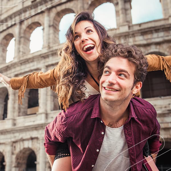 Mulher sorri nas costas do seu namorado enquanto passeiam em frente ao Coliseu em Roma