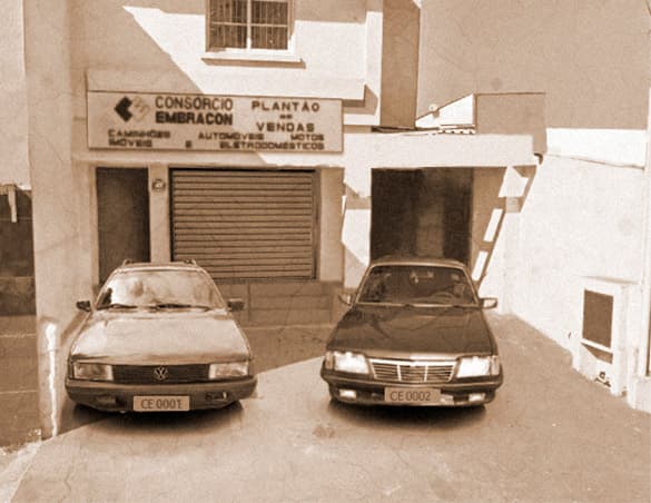Dois veículos parados em frente à primeira sede do Consórcio Embracon, foto em preto e branco